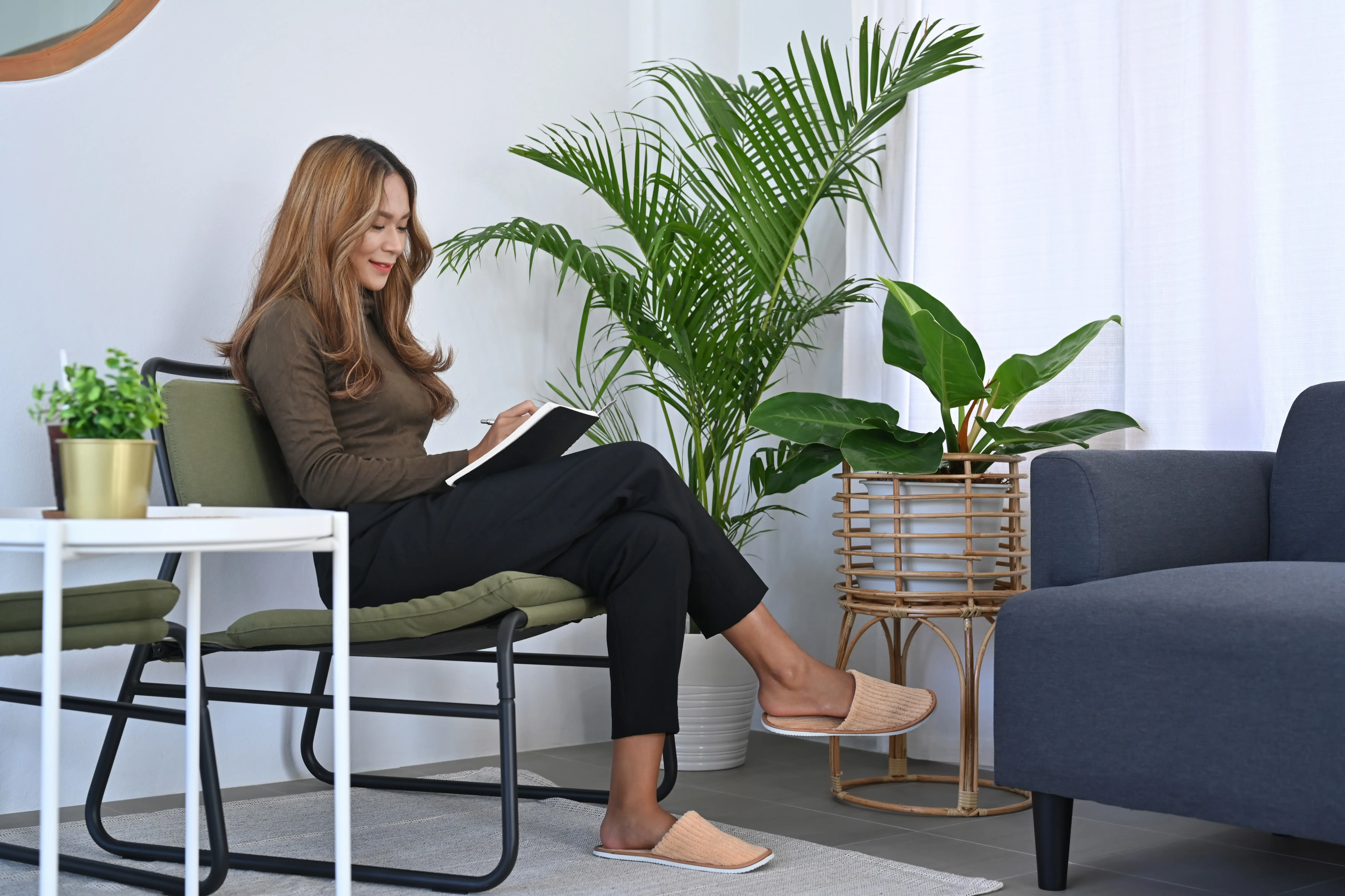 Ganzkörperporträt einer lächelnden Frau, die im Wohnzimmer auf einem bequemen Stuhl sitzt und ein Buch liest.